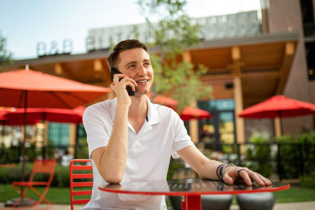 Homme souriant, téléphone à l'extérieur, terrasse ensoleillée.